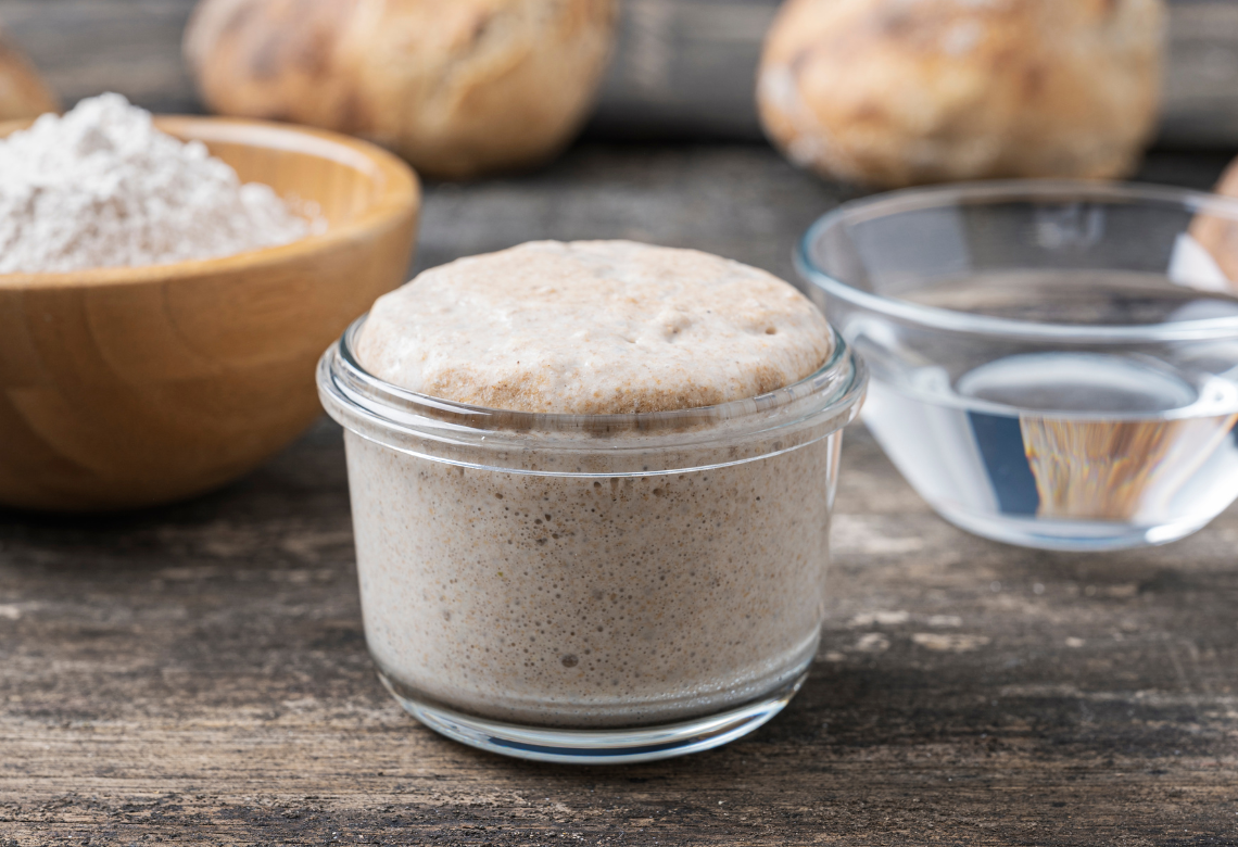 Mature sourdough starter in a jar, doubled in size with bubbles and domed top