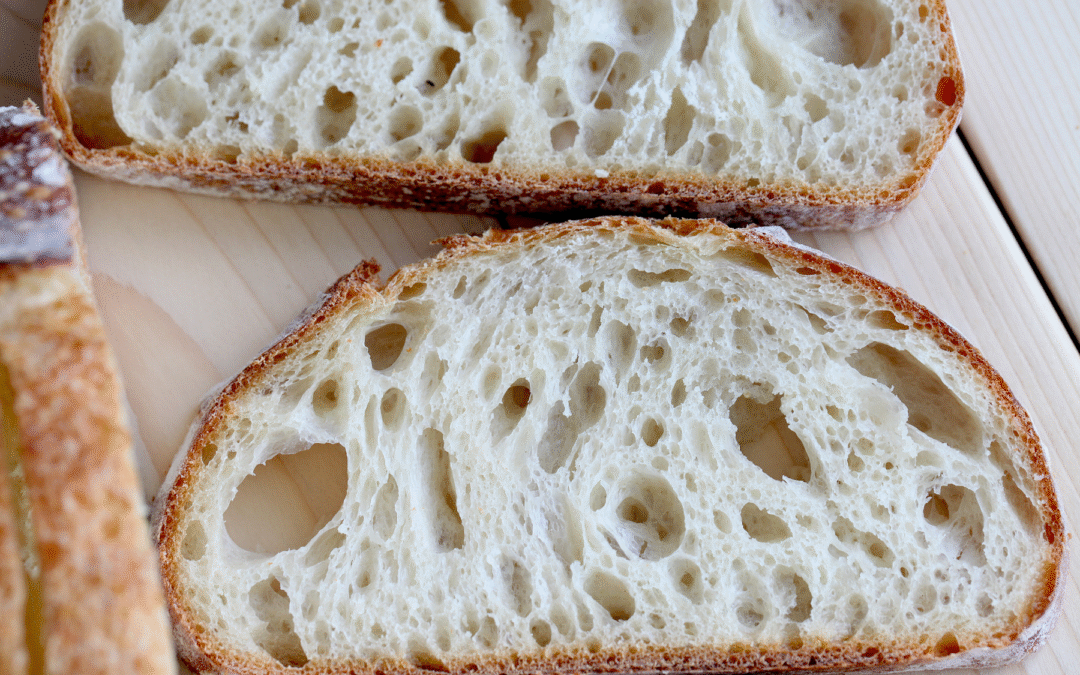 Close-up of sliced sourdough bread showing an open, airy crumb structure on a cutting board.