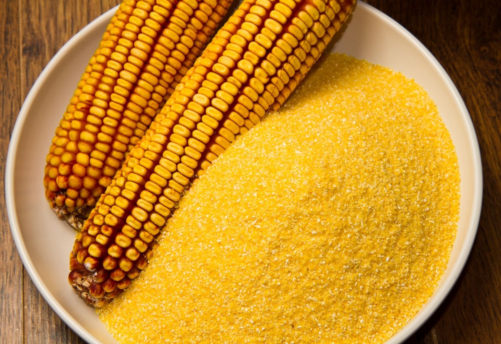 Yellow cornmeal and fresh corn kernels displayed on a plate, the main ingredient used in making sourdough cornbread and corn muffins.