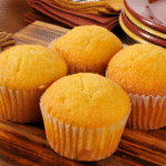 Golden bakery style honey corn muffins in white liners displayed on a wooden board.
