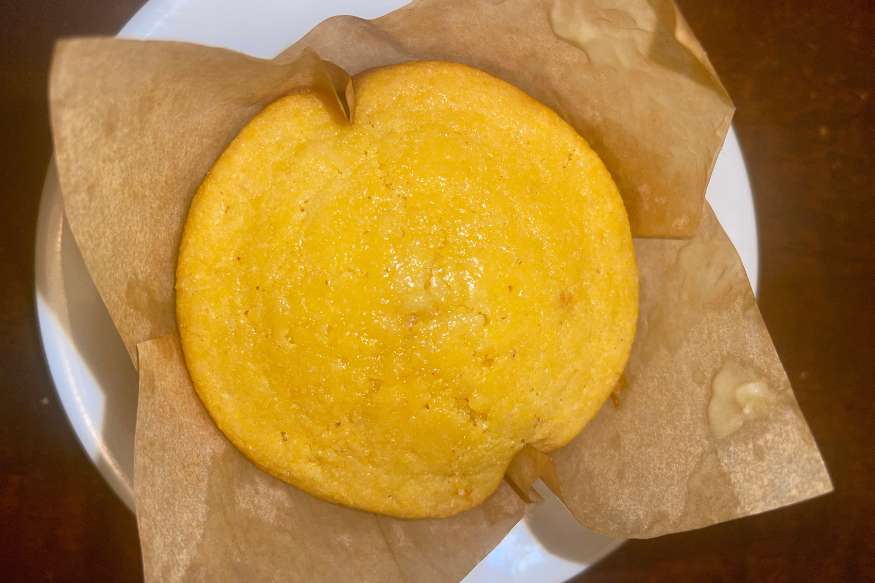 Close up of one honey sourdough corn muffin in a tulip liner with a shiny honey butter glaze.