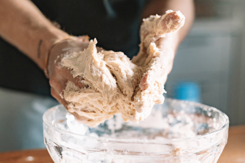 Close-up of sticky sourdough dough stretching between hands on a white countertop, showing the elastic texture and early hydration stage during mixing.