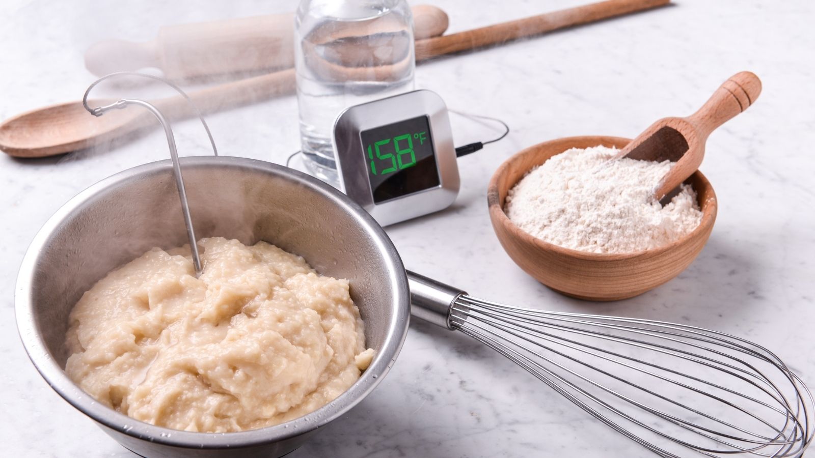 Tangzhong Starter Paste at 158°F A bowl of freshly cooked tangzhong paste at 158°F, with a thermometer, whisk, flour bowl, and baking tools in the background, demonstrating the gelatinized mixture used to create extra-soft bread.