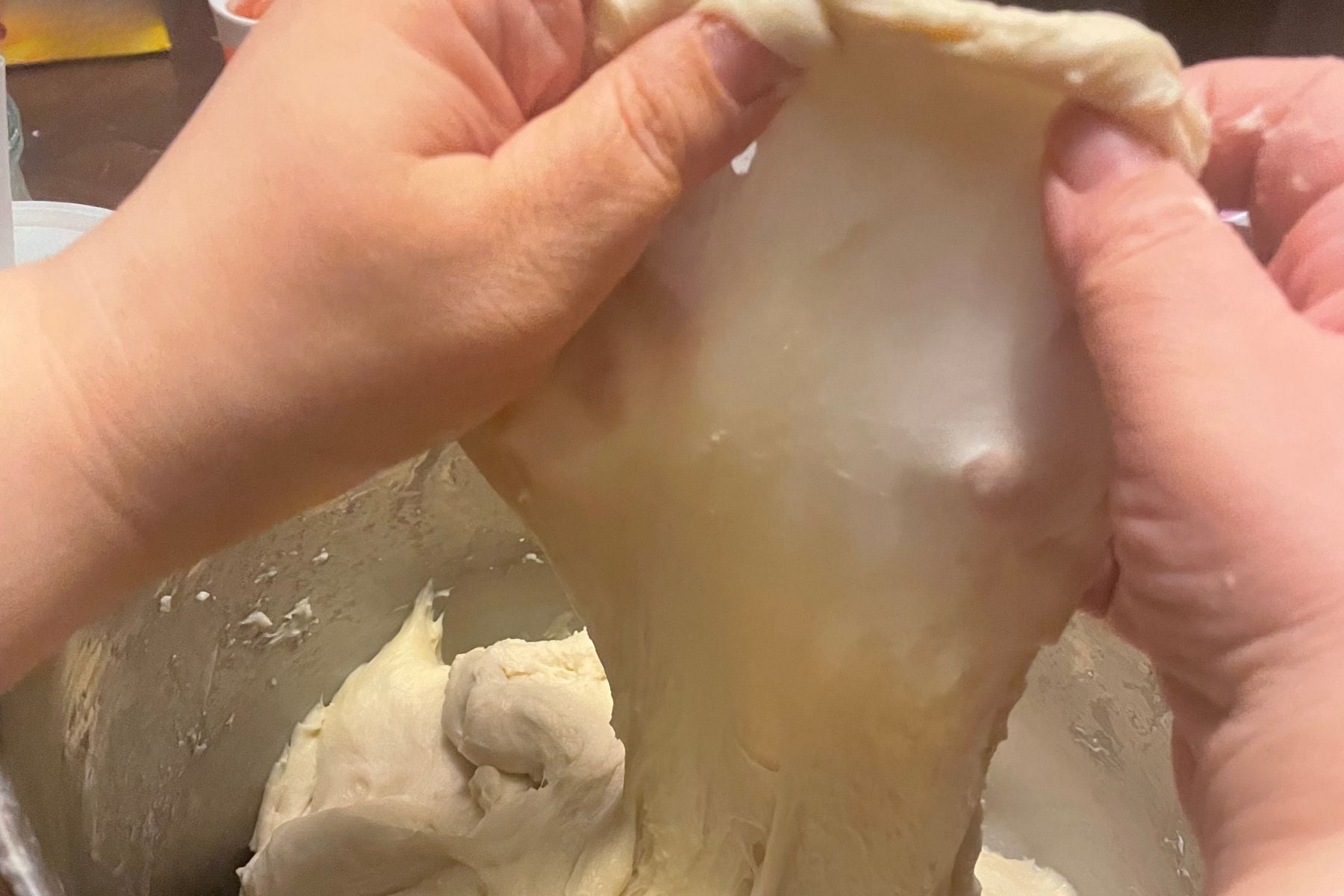 Hands stretching sourdough dough to show a clear windowpane, demonstrating gluten strength in a beginner sourdough bread recipe.