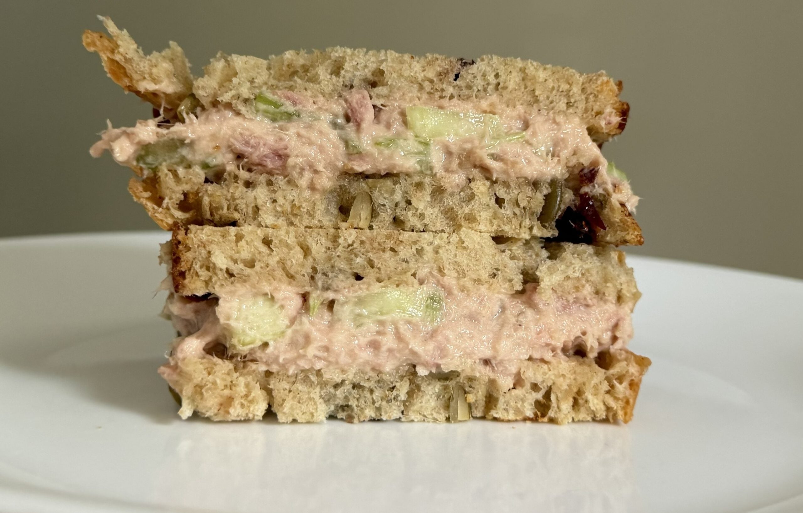Tuna sandwich made with cranberry pumpkin seed sourdough sandwich bread, served with sliced cucumbers and a glass of iced tea.